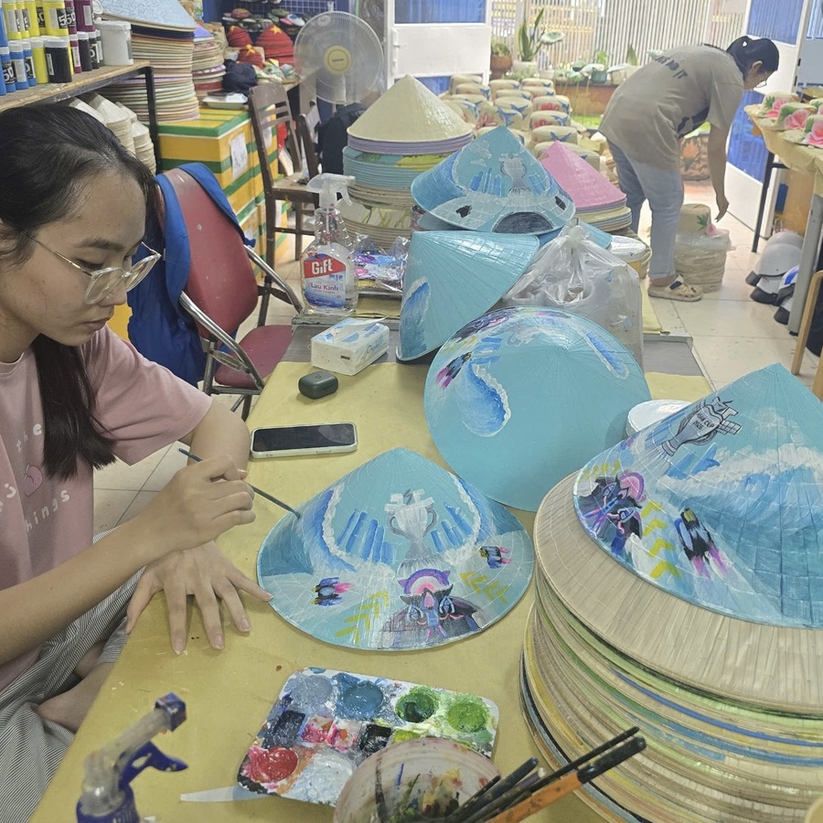Artisan hand-painting a blue conical hat with a custom design at the workshop