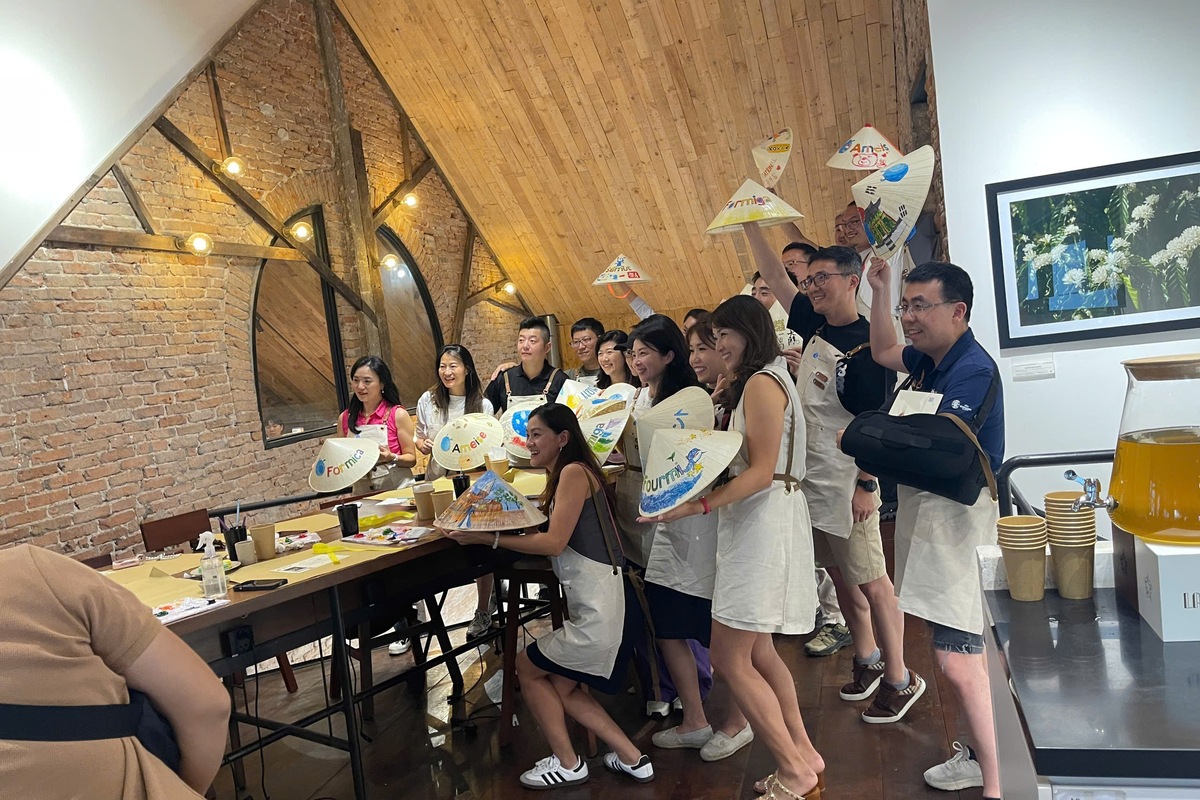 Corporate team members painting conical hats together during a company workshop in Ho Chi Minh City