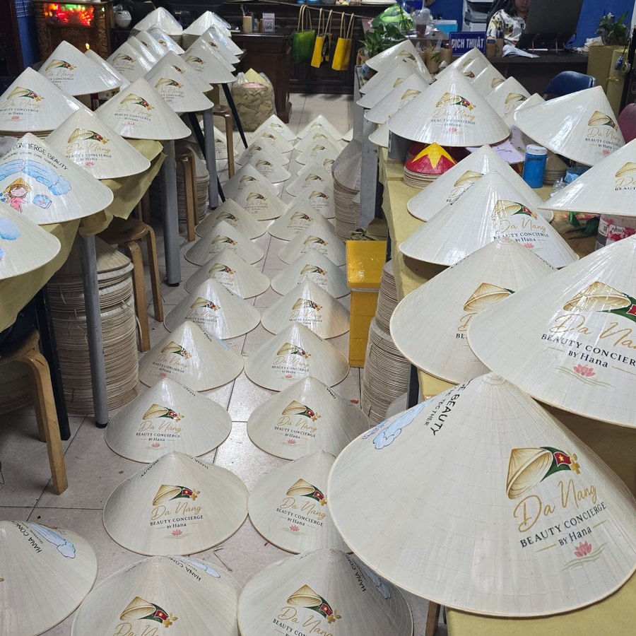 Rows of conical hats printed with a company logo for a bulk corporate order in a Saigon workshop